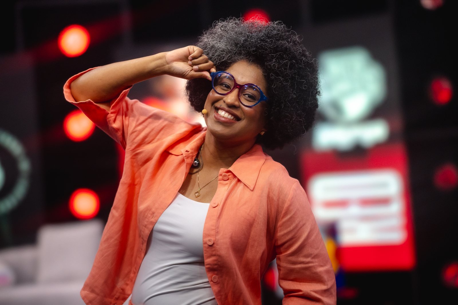 Lahgolas sorrindo durante uma transmissão, usando camisa coral e óculos coloridos.